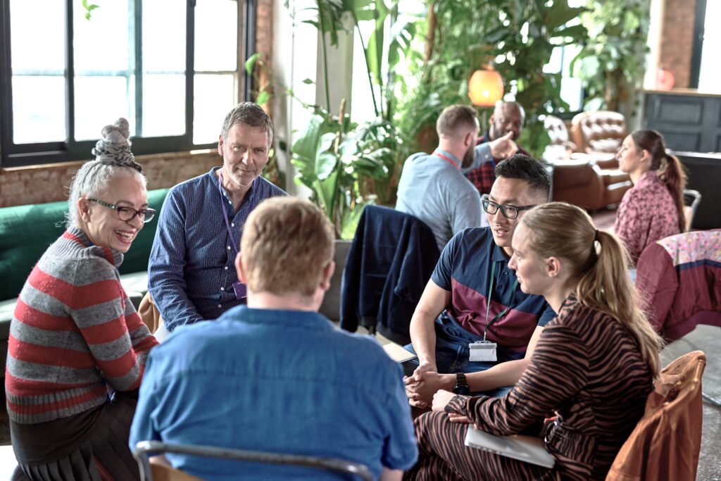 Group of people of different ages sitting in a circle in a public space having a discussion.