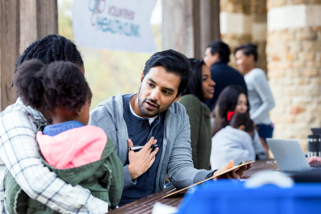Man with a clipboard giving advice to a woman and a child in her lap at a health event.